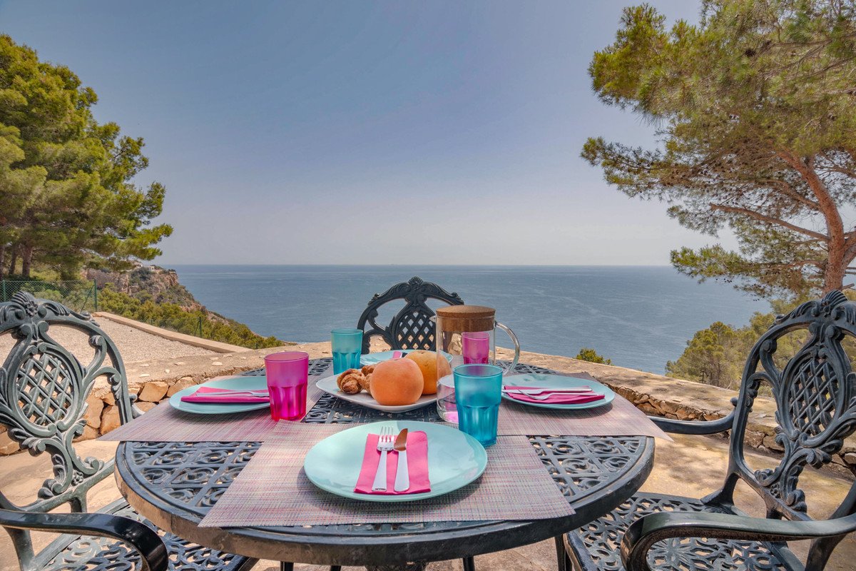 Outdoor dining table set for breakfast with colorful glasses and a beautiful sea view from the terrace.