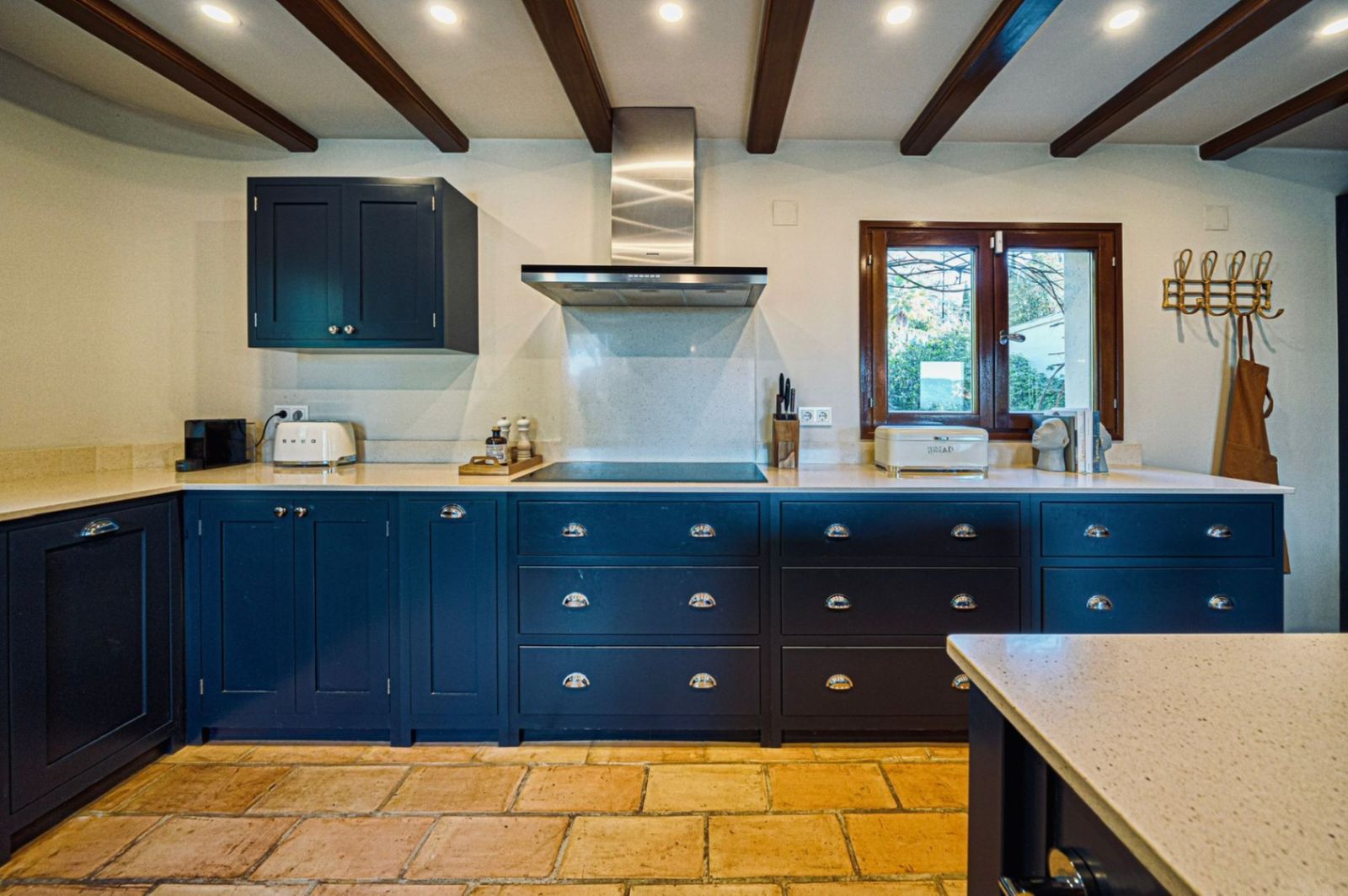 Rustieke keuken met blauwe kasten, houten balken en terracotta vloer.