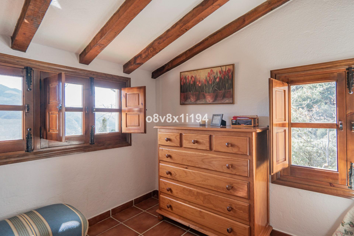 Rustieke slaapkamer interieur met houten balken, commode en ramen met uitzicht.