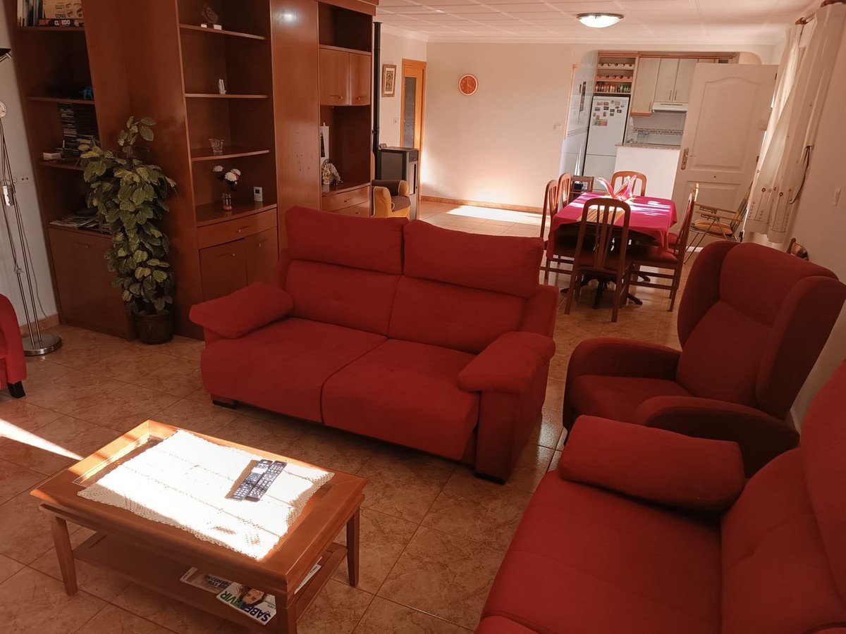 A spacious living and dining area with red sofas, armchairs, a coffee table, and a dining table with chairs visible in the background.