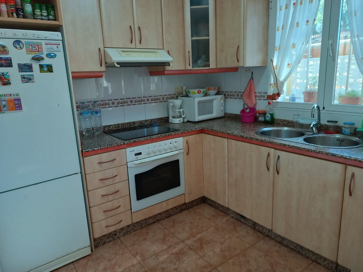 A bright kitchen with light wood cabinets, a white oven, stove, refrigerator, microwave, and sink by a window.