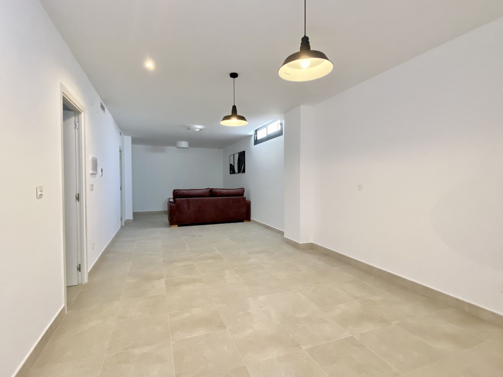 Modern interieur van een woonkamer met een donkerrode bank en hanglampen.