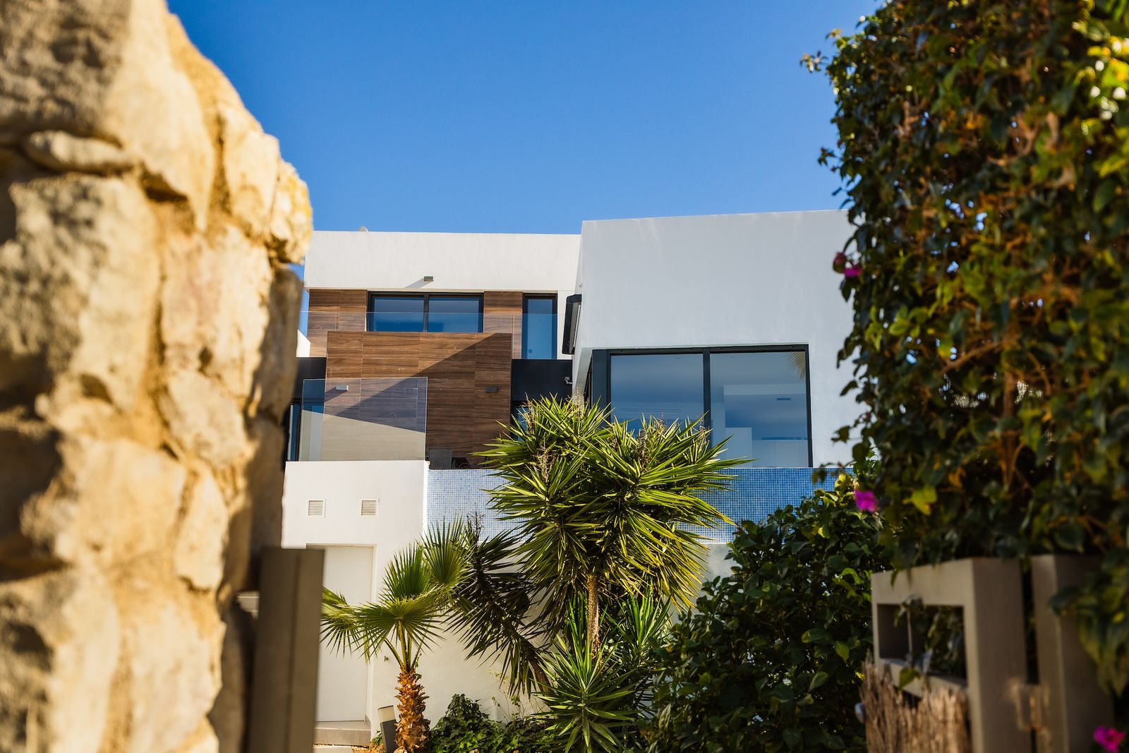 Exterieur van een moderne villa met weelderige tuin en heldere blauwe lucht.