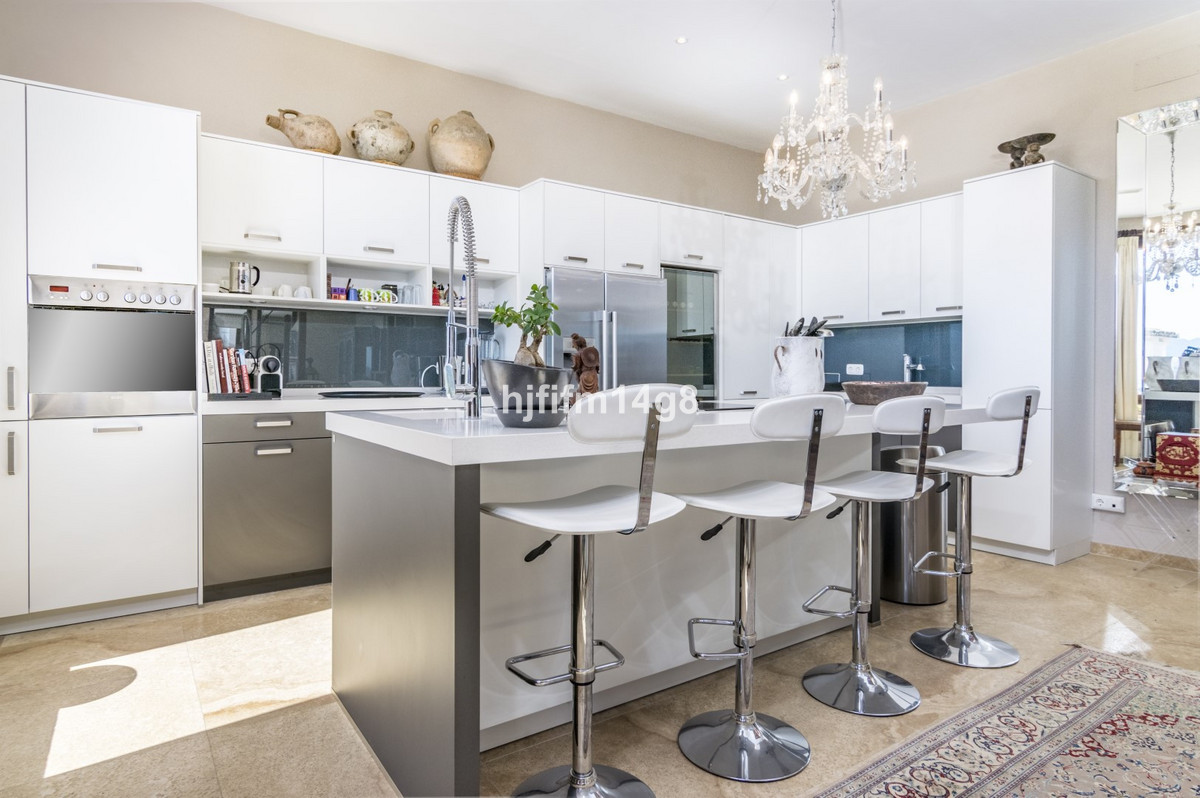 Moderne keuken met eiland, witte kasten en chromen barkrukken.