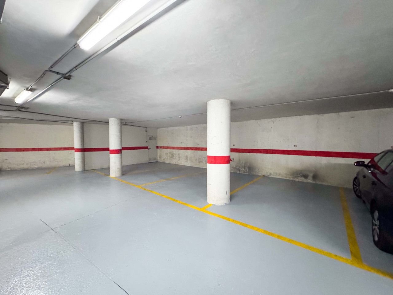 Empty parking garage with white pillars, red and yellow lines, and fluorescent lighting.
