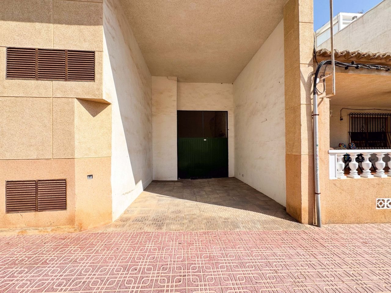 Courtyard with beige walls, green door, and patterned floor.