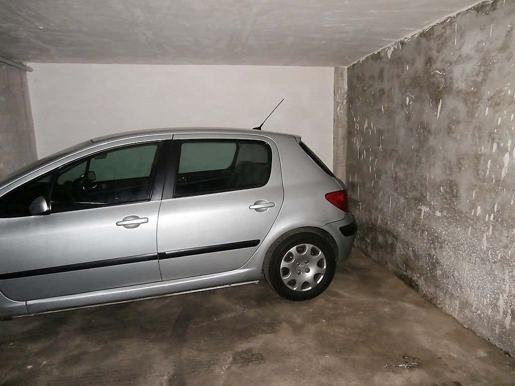 Small garage with concrete walls and floor, silver car parked inside.