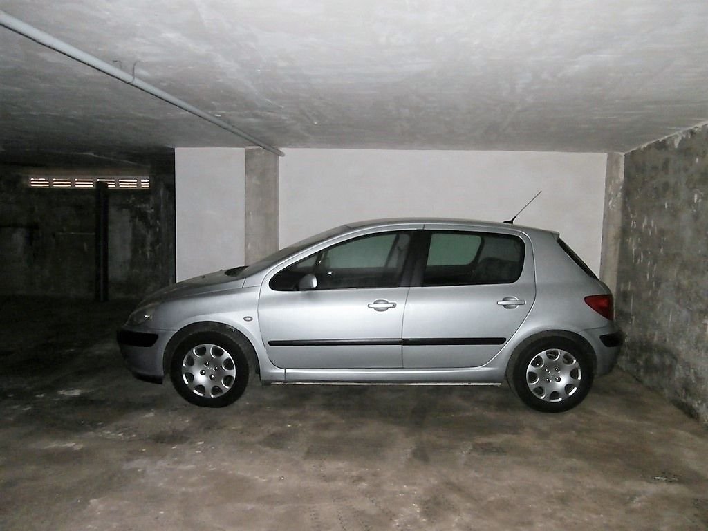 A silver hatchback car parked in a dimly lit garage with concrete walls.