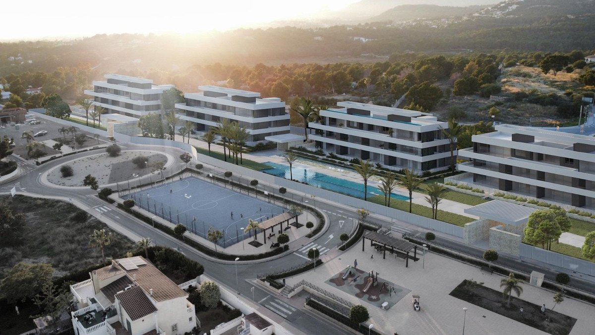 Modern apartment complex with pool, tennis court, and playground at sunset.