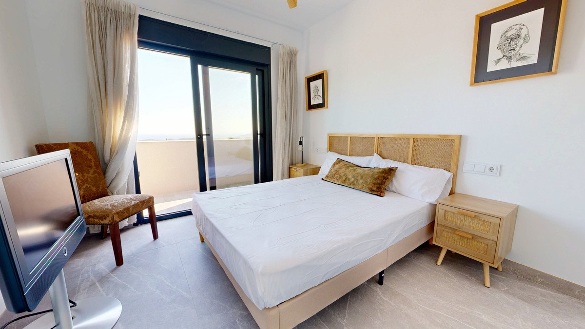 Bedroom with a large bed, a bedside table, a chair, and a balcony with a distant sea view. Modern and a TV.
