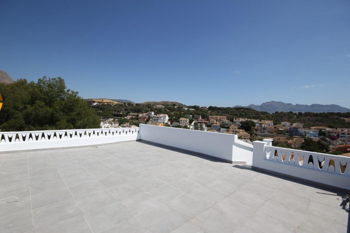 White rooftop terrace with view of town and mountains under clear blue sky