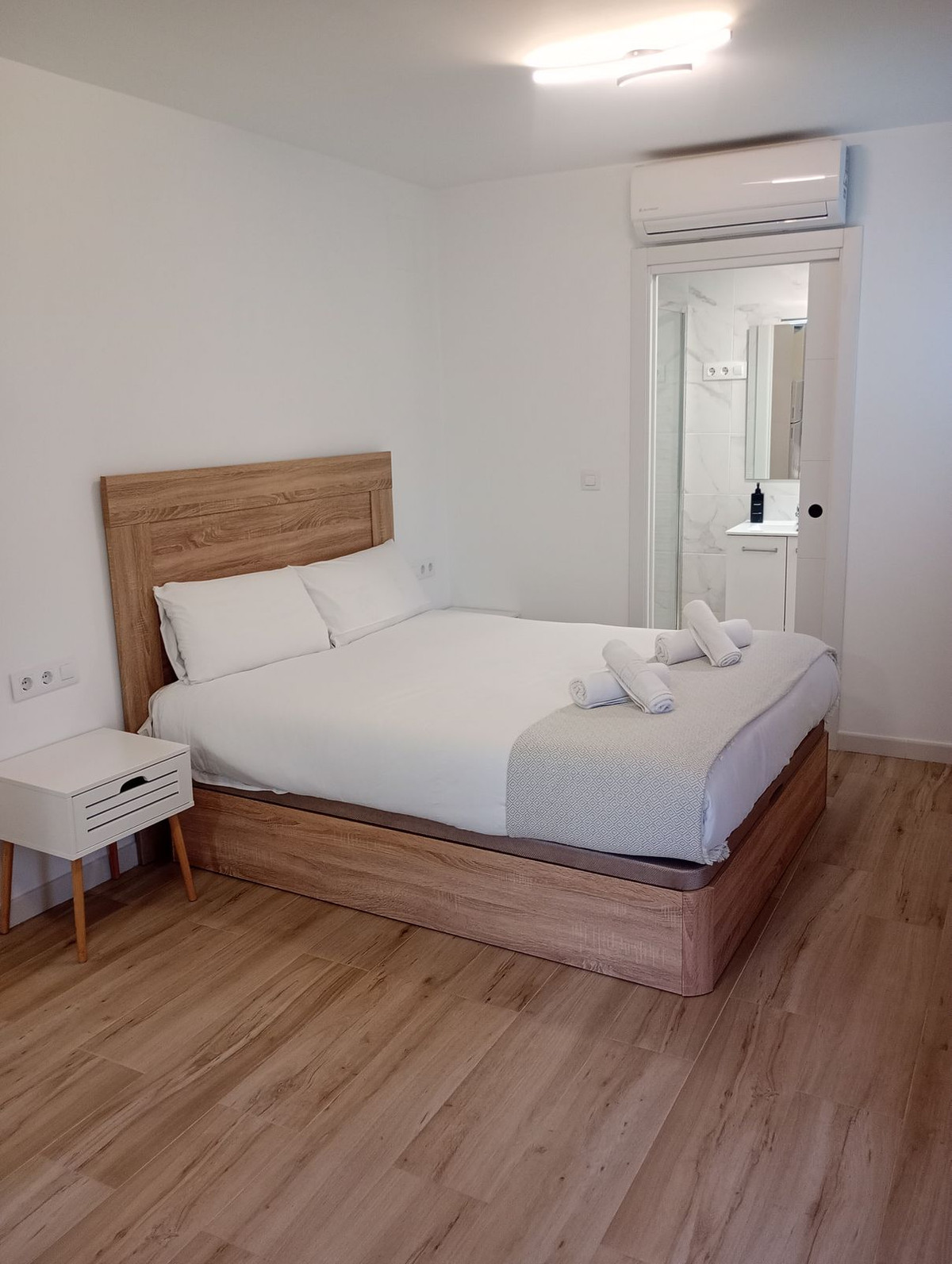 Moderne slaapkamer met ensuite badkamer, houten bedframe en wit beddengoed.