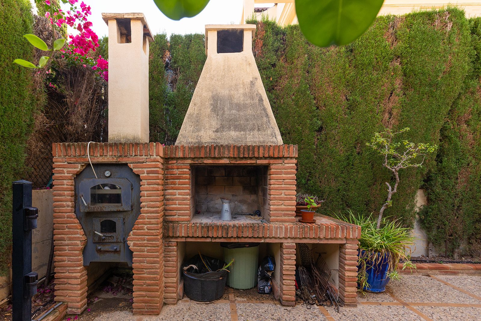 Buitenoven en barbecue van baksteen in een weelderige tuin.