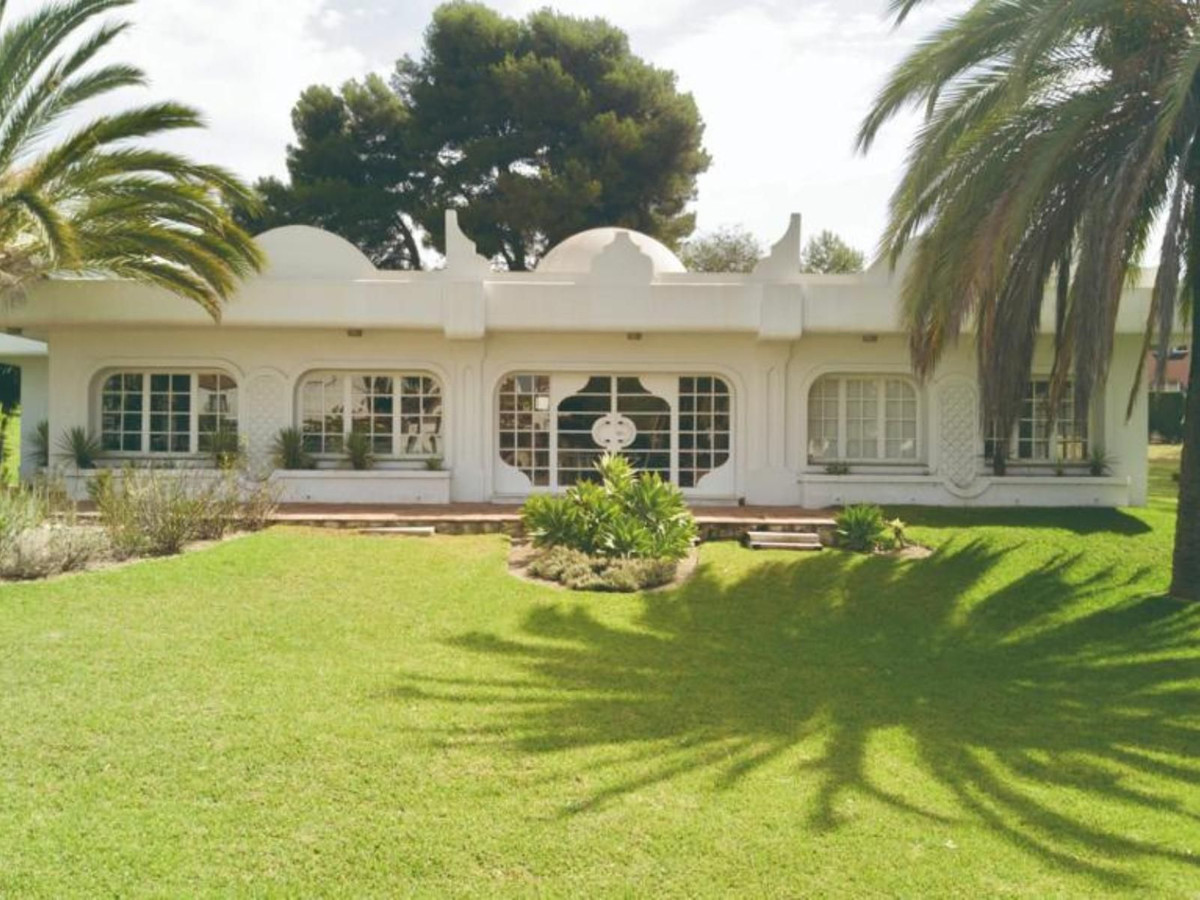 Buitenkant van een unieke witte villa met gazon en palmbomen.