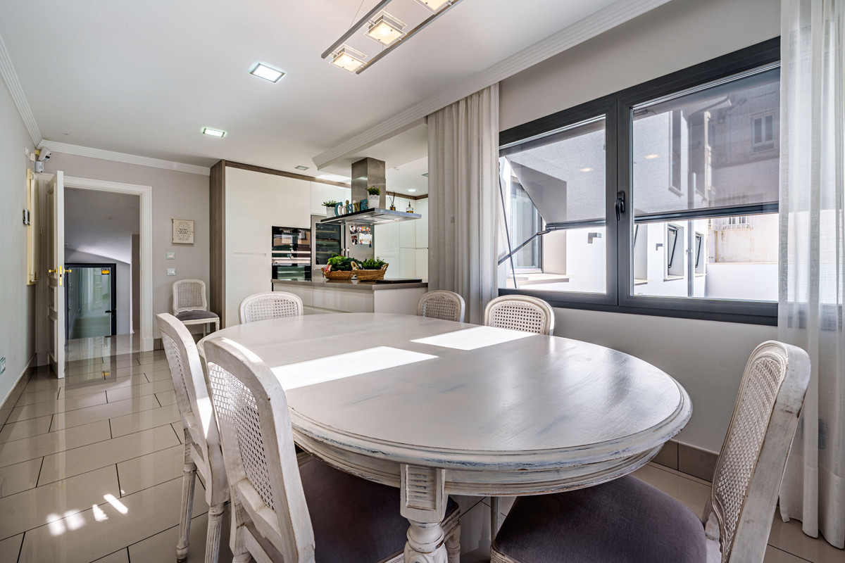 Eetgedeelte in open keuken met witte ronde tafel en rieten stoelen.