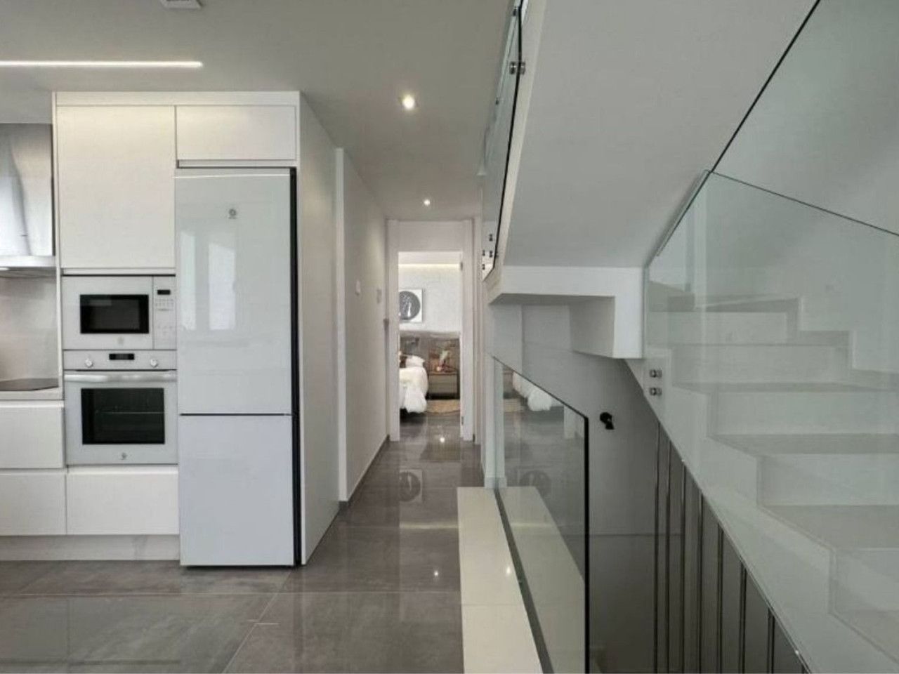 Modern interieur met witte keuken en trap met glazen balustrade.