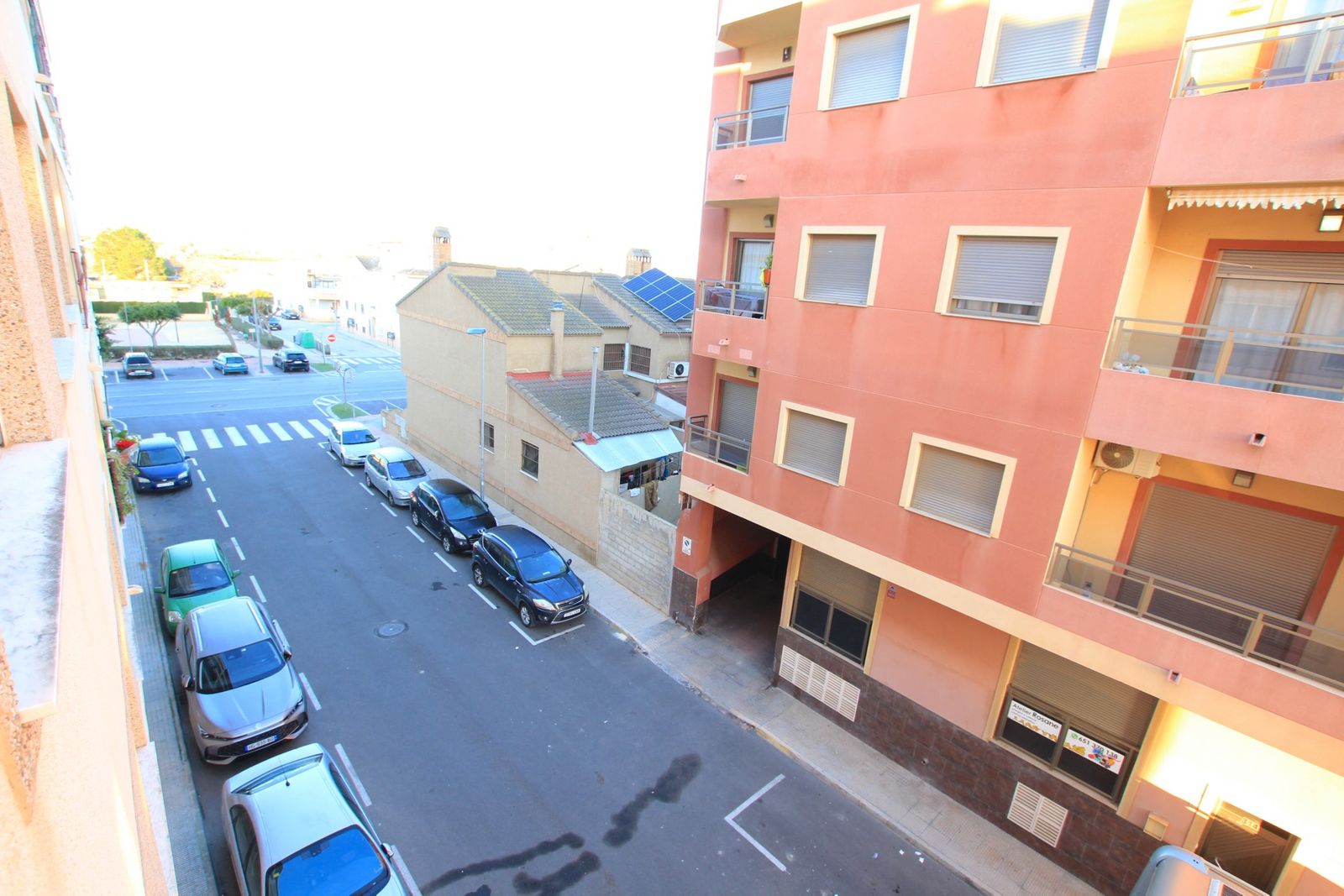 Straatzicht vanaf appartement met geparkeerde auto's en gebouwen.