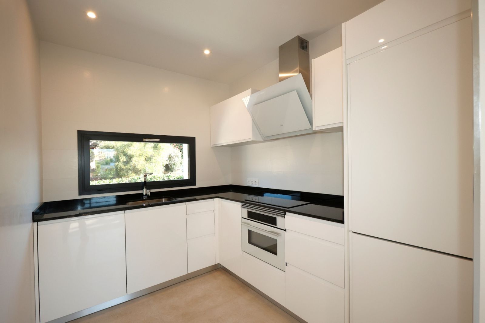 Moderne witte keuken met zwarte aanrechtbladen en uitzicht naar buiten.