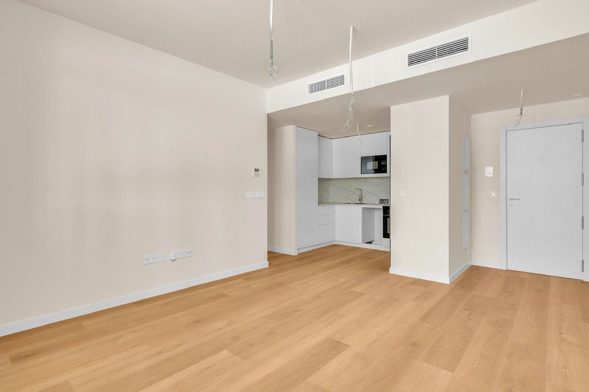 Empty room with wooden floors, white walls, and modern kitchenette.