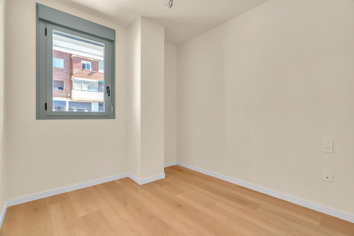 Empty room with wooden floor, large window, and white walls.