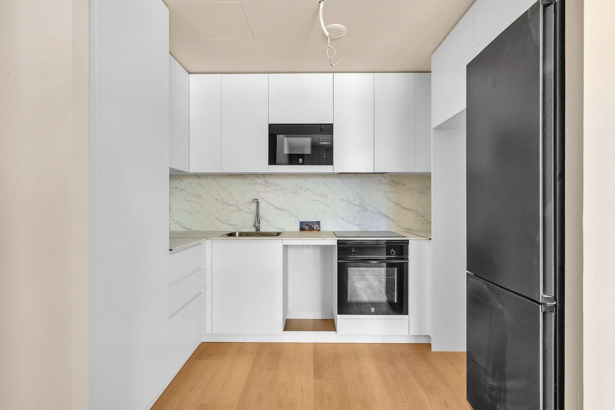 Modern kitchen with white cabinets, marble backsplash, black appliances, and wooden flooring.