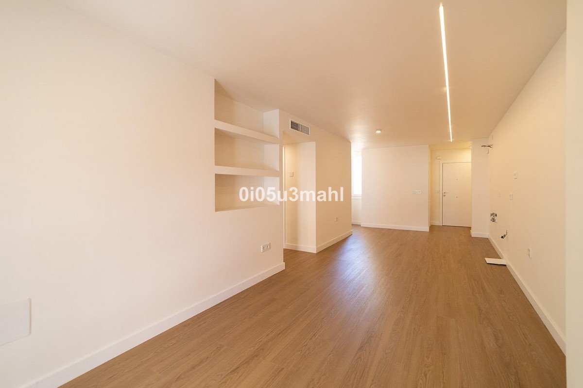 A spacious, empty modern living room with light wood floors and built-in shelves. Features recessed shelving and modern linear ceiling lighting.