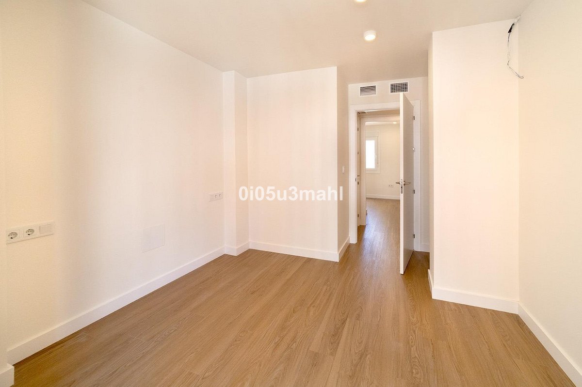 Empty room with wood flooring, looking down a hallway with doors leading to other rooms and a window in the distance.