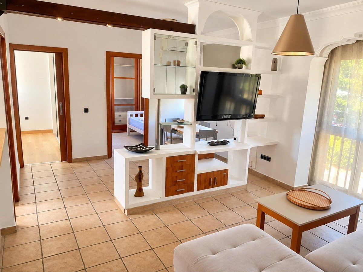 Living room with TV and shelves, featuring a view into a bedroom and dining area beyond.