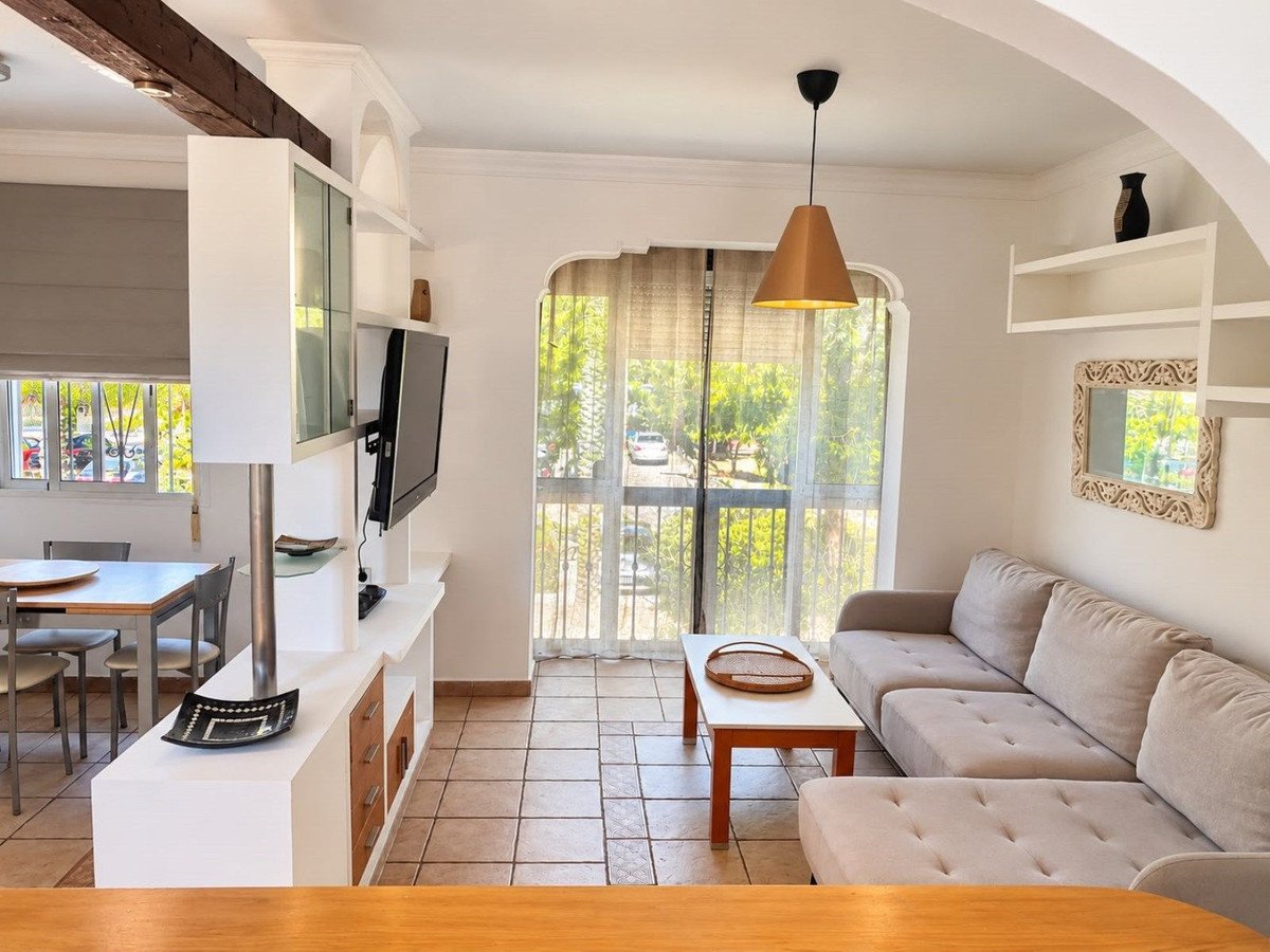 A modern living room with a sectional sofa, coffee table, and a balcony with a view of trees and a street.