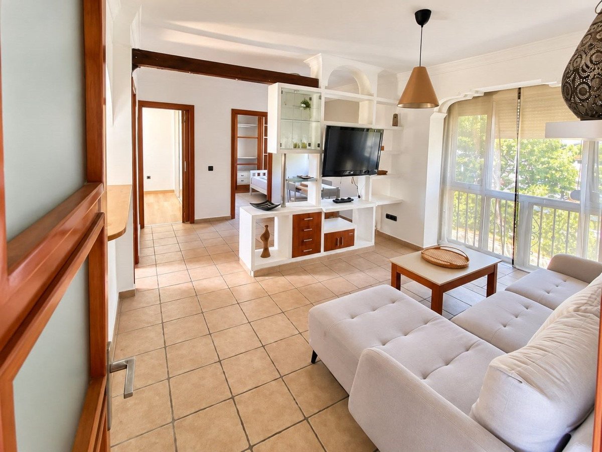 Bright living room with a white sectional sofa, TV unit, coffee table, and balcony doors with a green view.