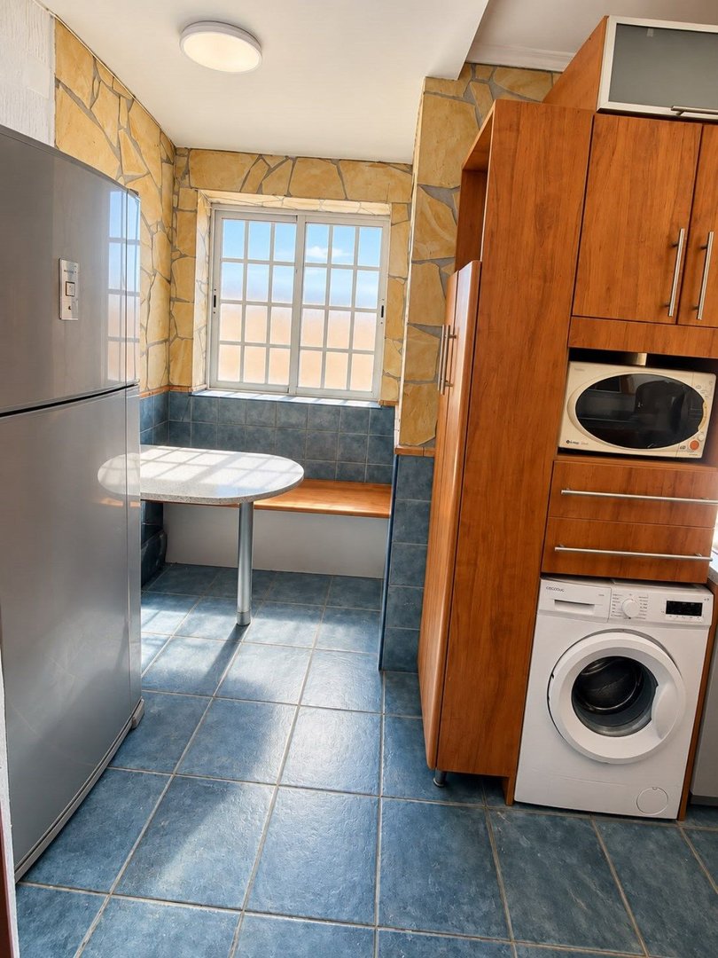 A small kitchen with a refrigerator, built-in seating, microwave, washing machine, and a large window with a grid pattern.
