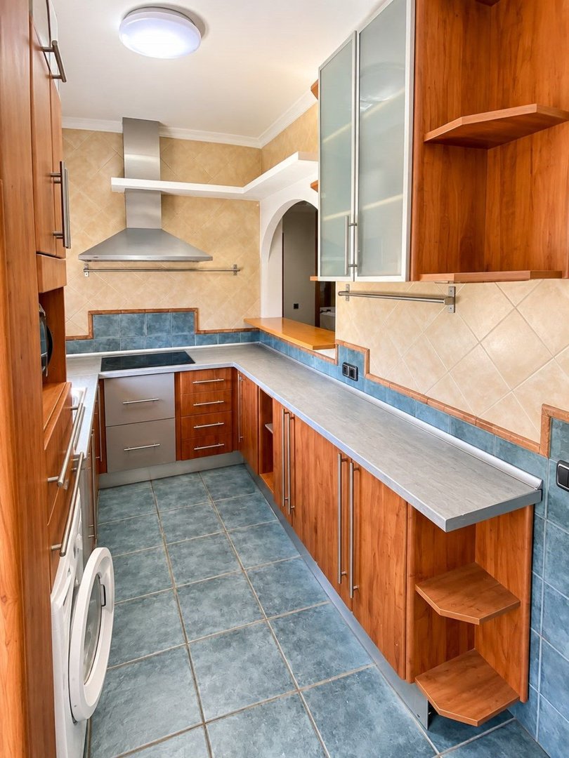 L-shaped kitchen with cherry wood cabinets, stainless steel appliances, tiled backsplash, and blue floor tiles. Includes washing machine.