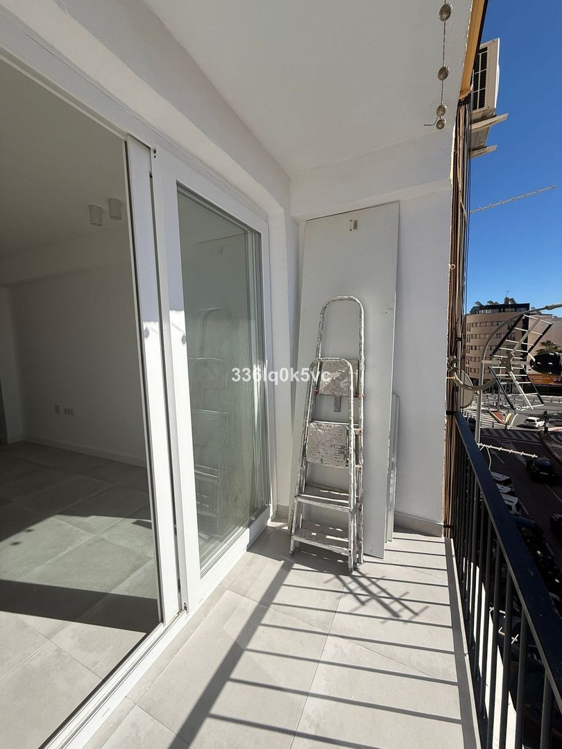 Balkon se skleněnými dveřmi, kovovým žebříkem, výhledem na město, dlážděnou podlahou.
