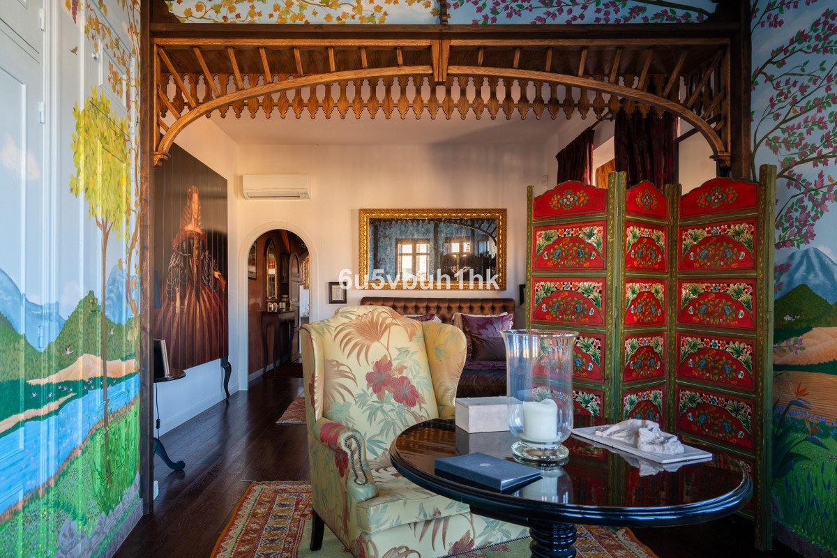 An ornate living room with a colorful screen, patterned armchair, and detailed murals on the walls.