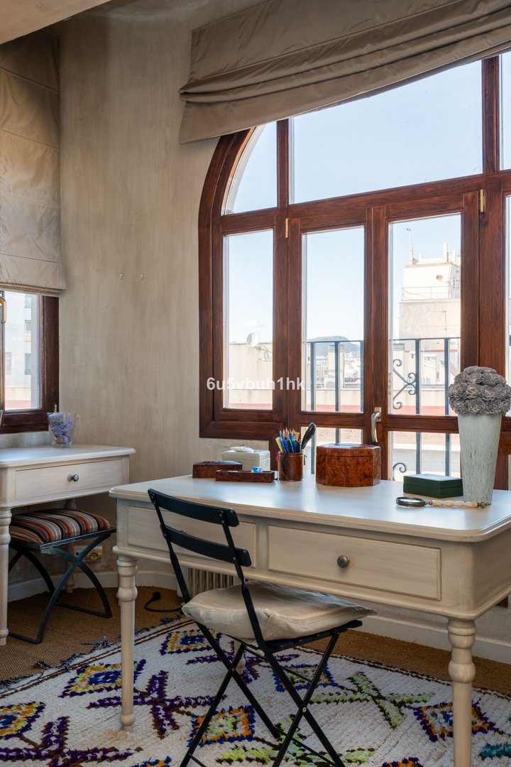 Study desk by a large window with a city view, featuring a colorful rug and organized workspace.