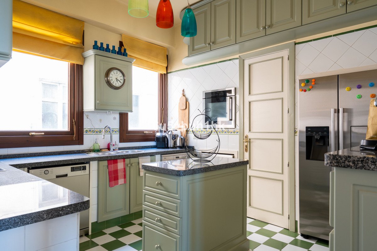 Modern kitchen with green cabinets, island, stainless steel appliances, checkered floor, and pendant lights.