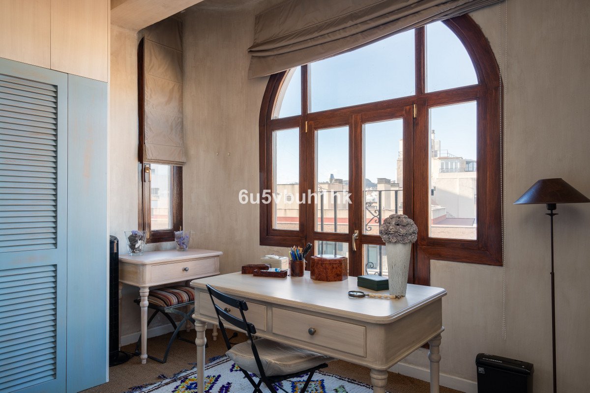 Cozy home office with two desks, arched wooden window offering city views, and a built-in wardrobe.