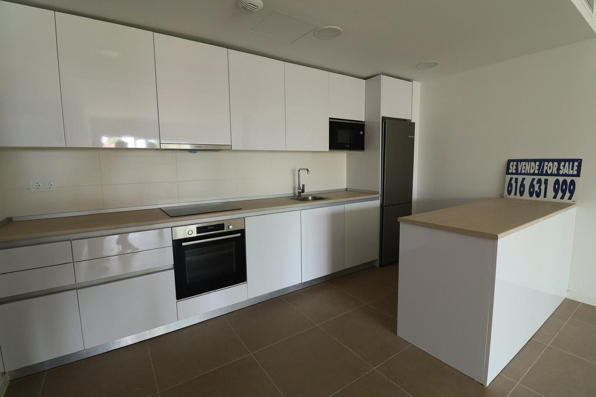 Modern white kitchen with integrated appliances, island, and a 'For Sale' sign visible.