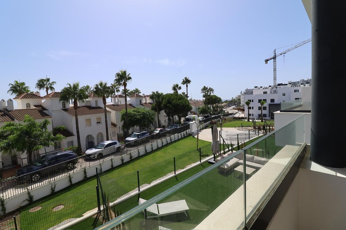 View from a balcony overlooking palm trees, white houses, parked cars, and a construction crane in the distance under a clear blue sky.