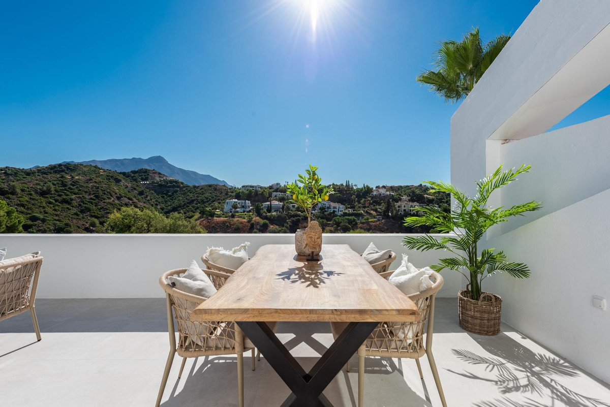 Outdoor dining area on a terrace with a table, chairs, and a beautiful mountain and town view under a bright sunny sky.