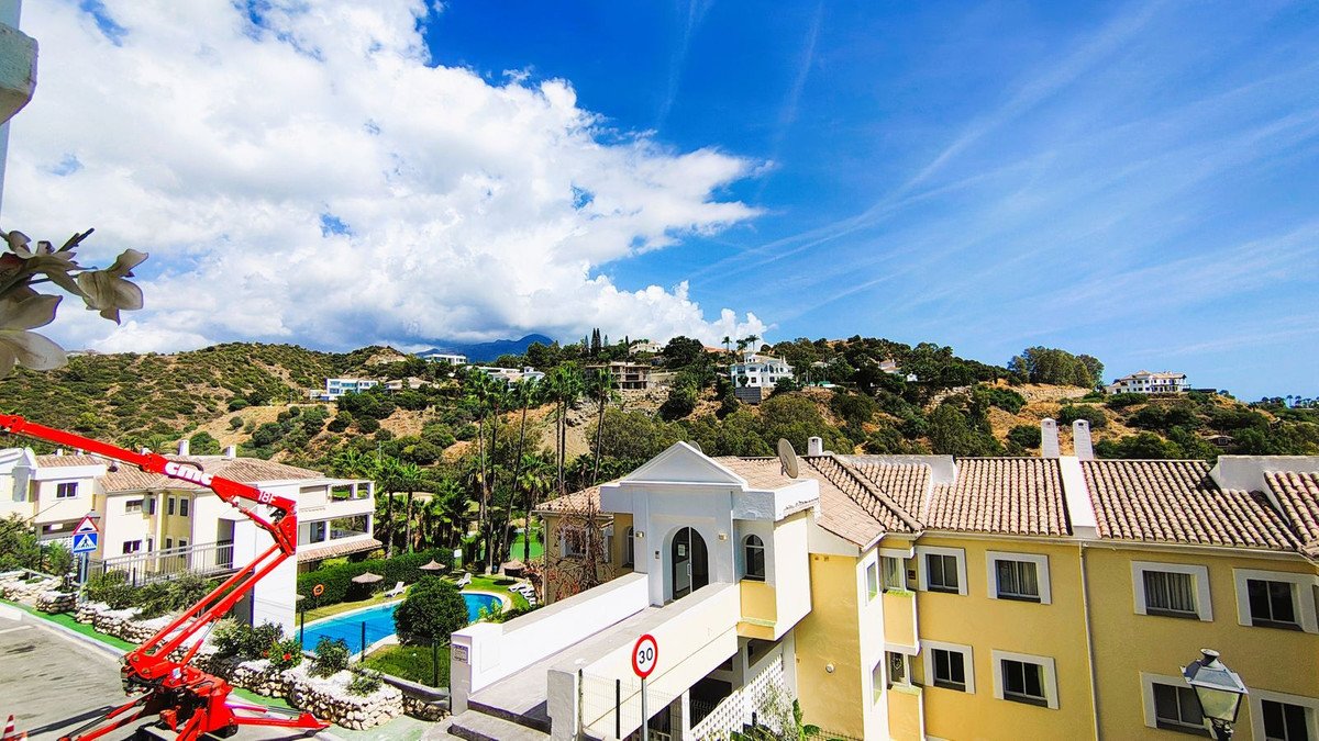 View of a swimming pool and residential buildings on a hillside under a blue sky with clouds.
