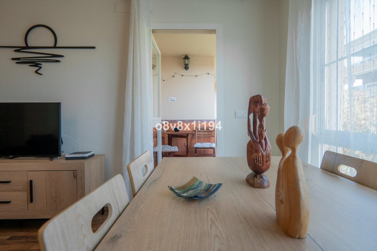 Dining area with wooden table, chairs, TV, and view into kitchen through doorway.