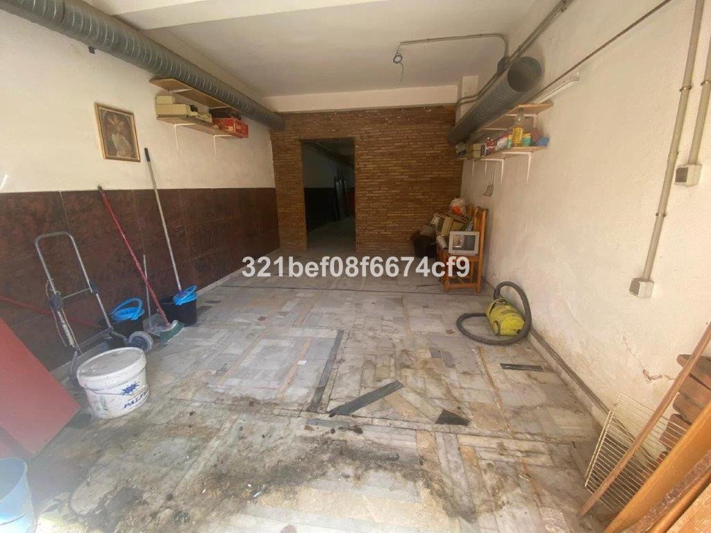 An empty interior space with cleaning supplies, including a vacuum, mops, and buckets. The walls have exposed brick and conduits.