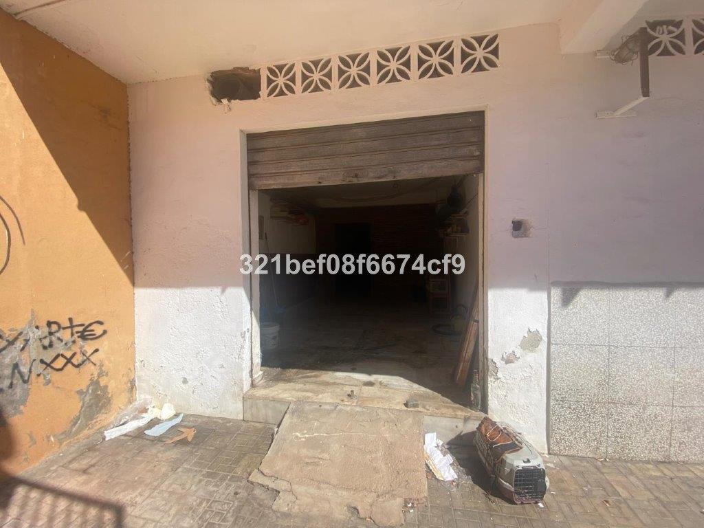 Exterior view of a commercial space with a metal shutter, showing a dilapidated entrance and graffiti on the wall.