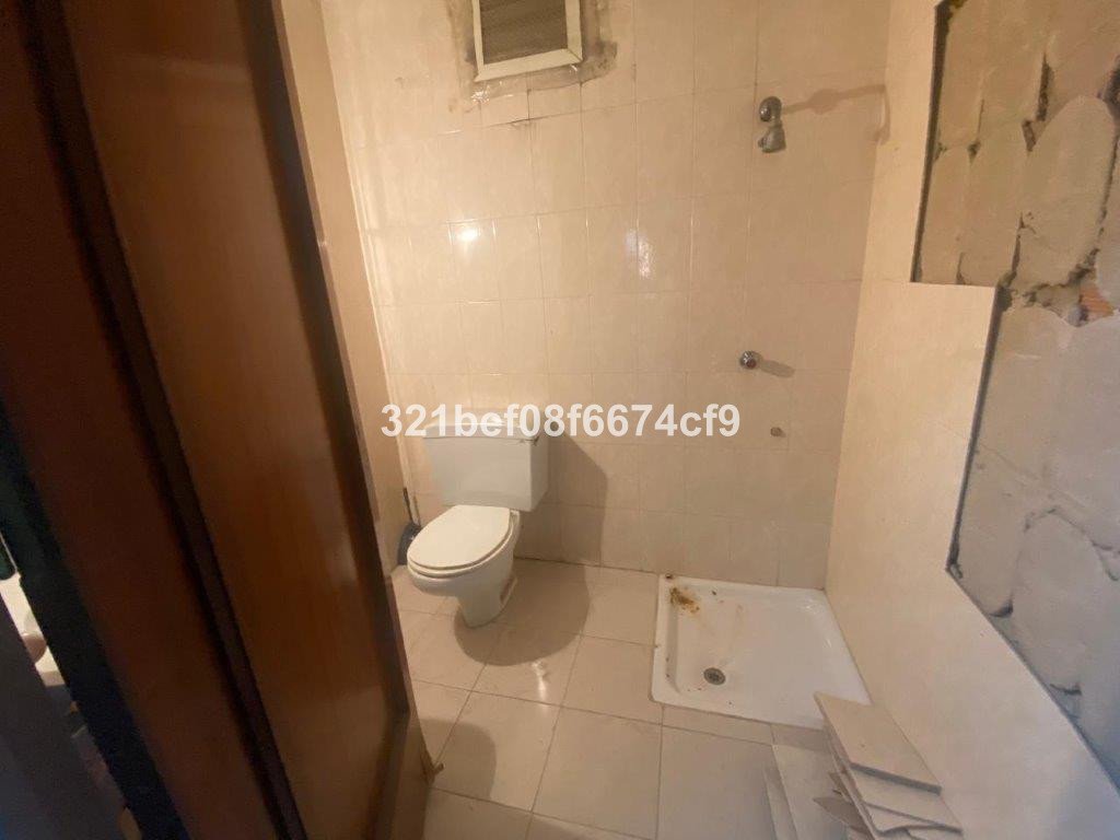 A bathroom with a toilet and a shower area, showing tiled walls and a small shower base.