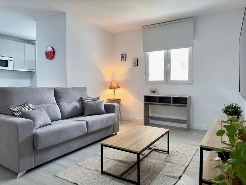 Modern living room with a grey sofa, coffee table, and a window with natural light.