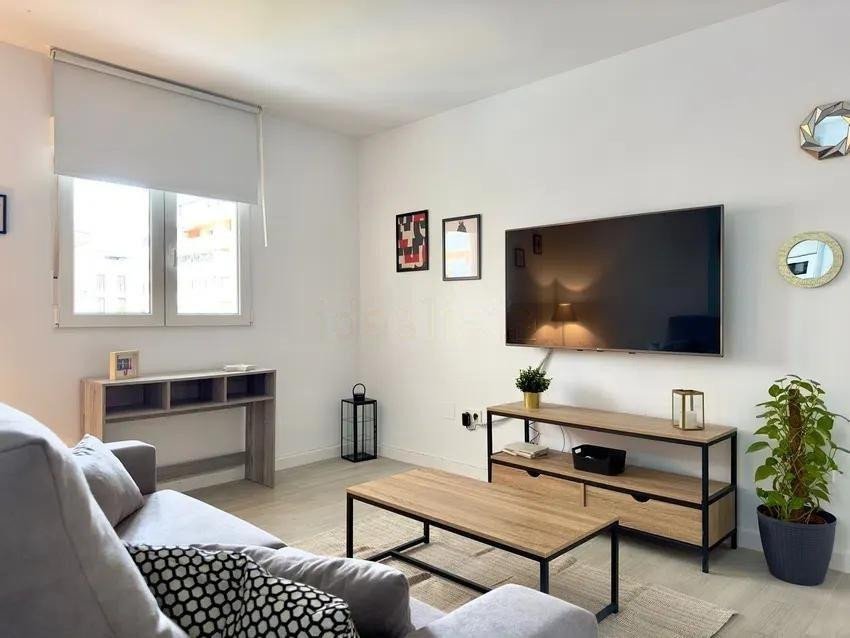 Modern living room with a grey couch, mounted TV, coffee table, and a window with roller blinds.