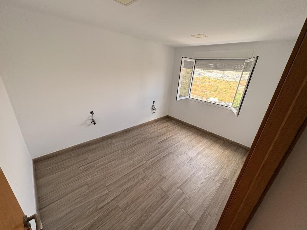 An empty room with light wood-look tile flooring, white walls, and a window with a view of an urban landscape.