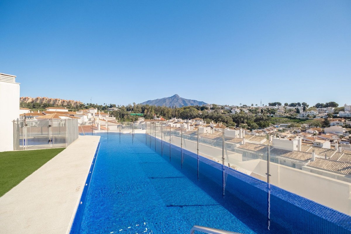 Infinity swimming pool on a rooftop terrace with stunning mountain views and a charming town below.