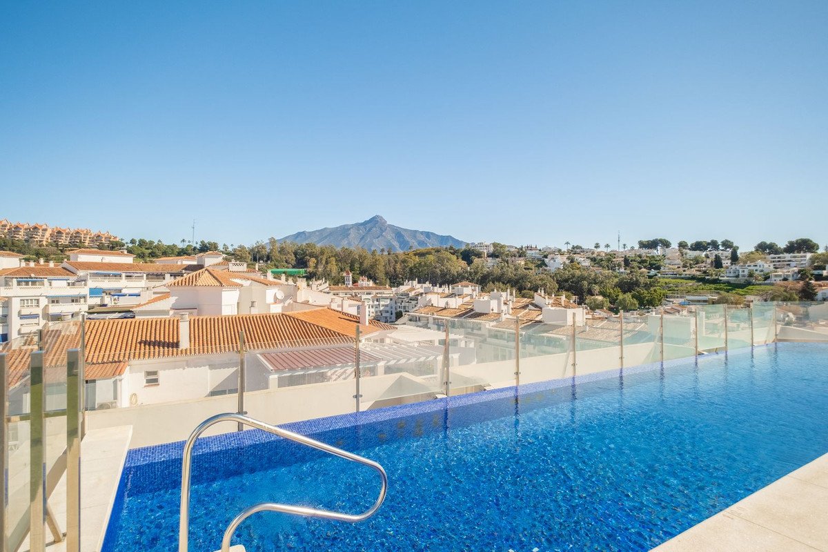 Infinity swimming pool with mountain and town view under a clear blue sky.